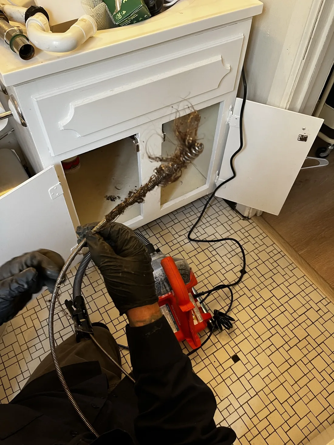 Técnico de Act Now Pros destapando una línea de drenaje de baño obstruida con una máquina de limpieza de drenajes
